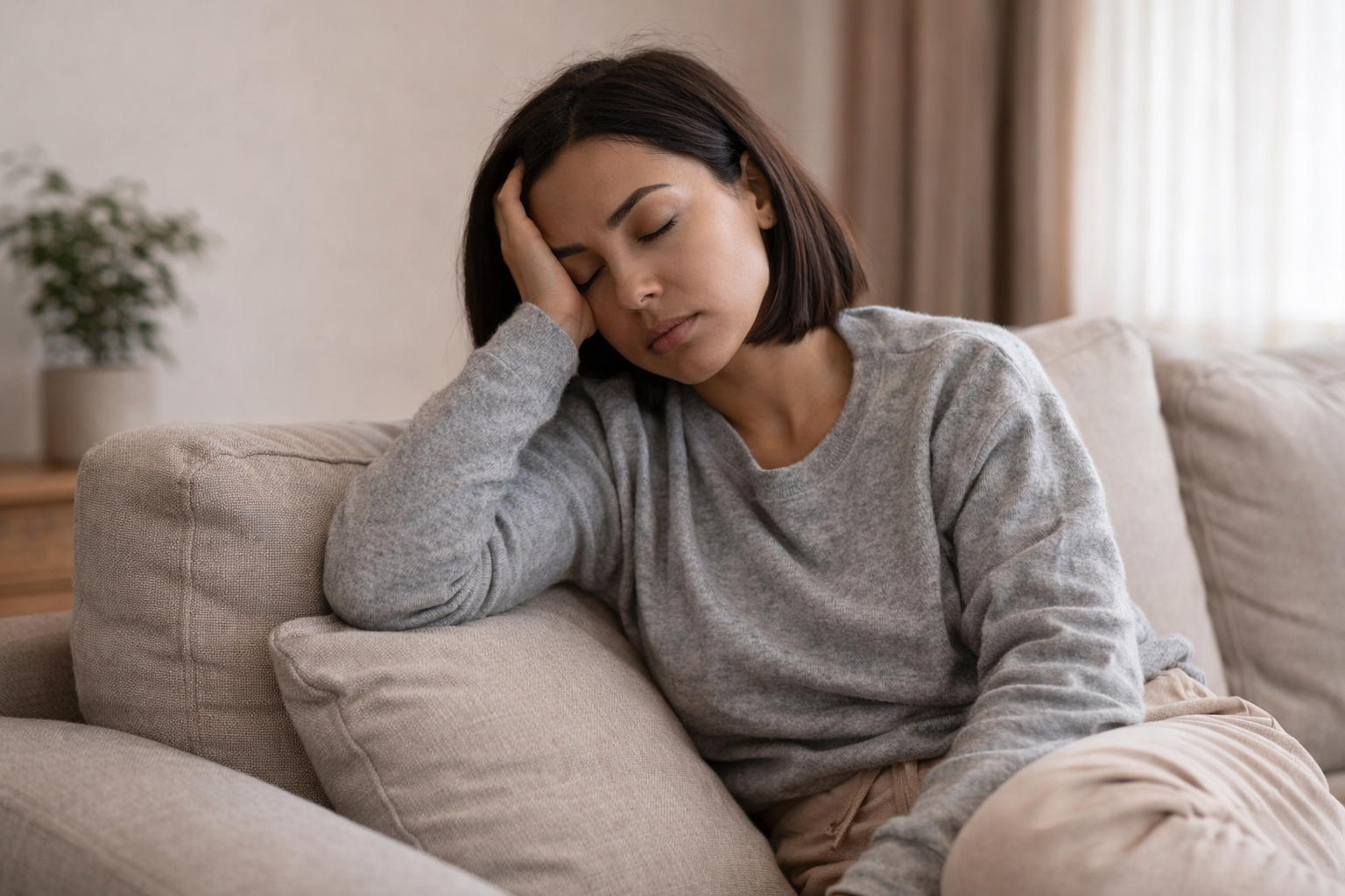 Woman feeling tired sitting on a couch at home, resting her head with low energy despite rest
